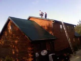Crew on the ridge of a green metal roof on a two story log home in Mesa